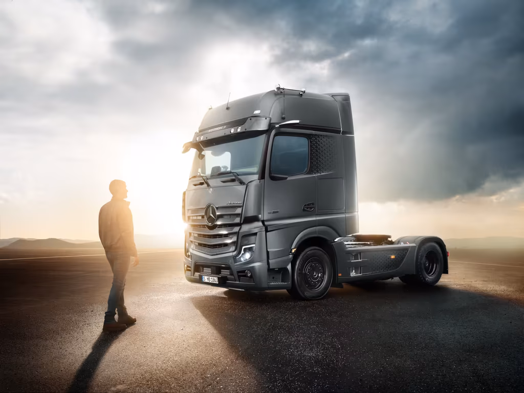 Ein Fahrer steht vor einem schwarzen Mercedes-Benz Lastkraftwagen auf einer Straße bei Sonnenuntergang.