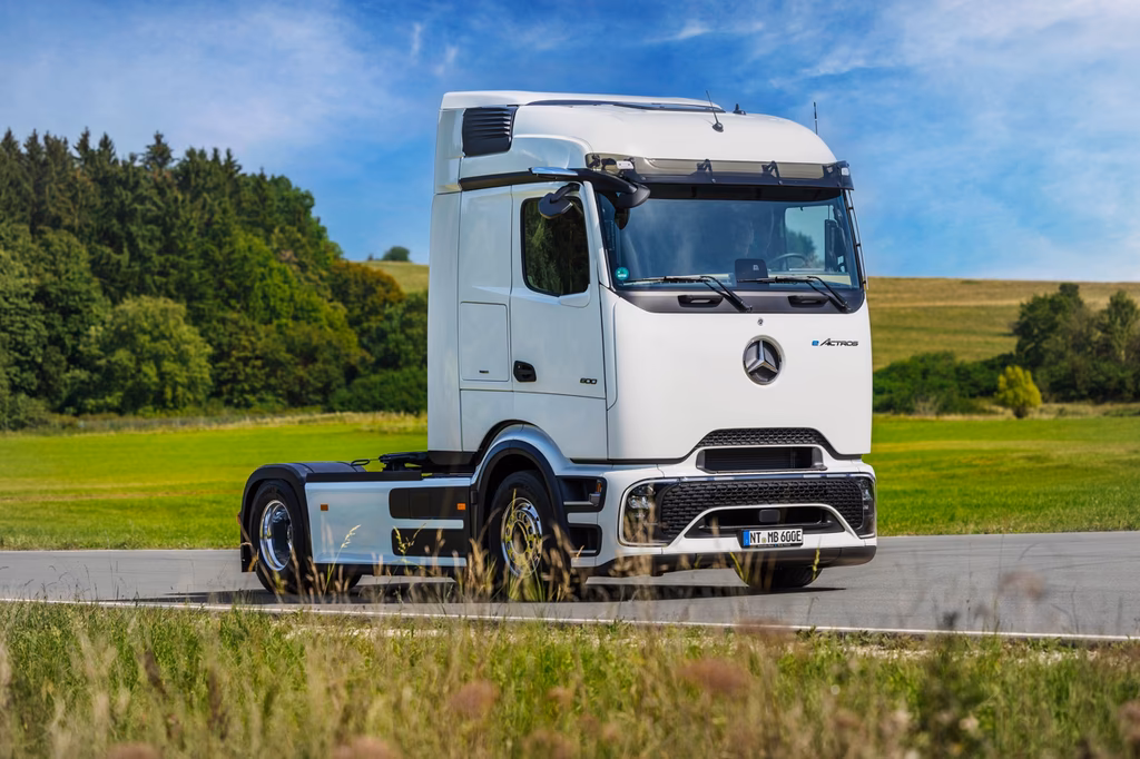 Weißer Mercedes-Benz eActros Elektro-Lastkraftwagen auf einer Landstraße mit grüner Landschaft im Hintergrund.
